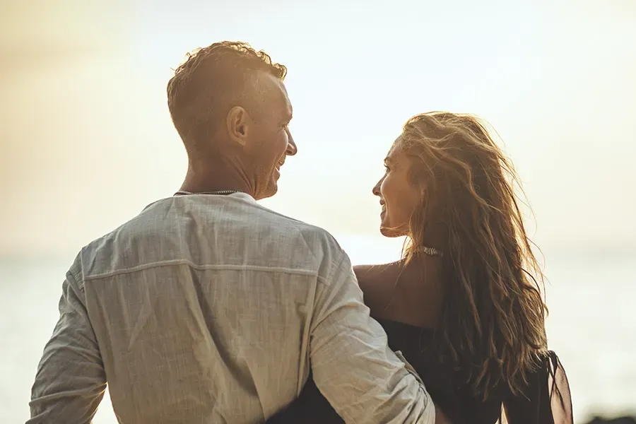 Anti-Aging-Clinic A couple gazes at each other on the beach at sunrise, viewed from behind. Schedule Anti-Aging treatment from Morgan Burns, APRN in Central Florida.