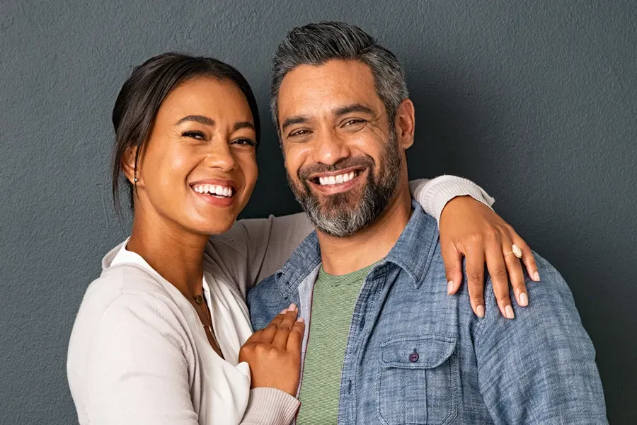 Bioidentical-Hormone-Therapy-Doctor A middle-aged couple with their arms around each other standing against a gray background and smiling, happy with the bioidentical hormone therapy they received from Morgan Burns, APRN in Central Florida.