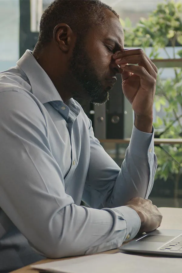 Chronic-Fatigue-Treatment A black man rubbing the top of his nose at his desk, in need of chronic fatigue treatment from Morgan Burns, APRN in Central Florida.