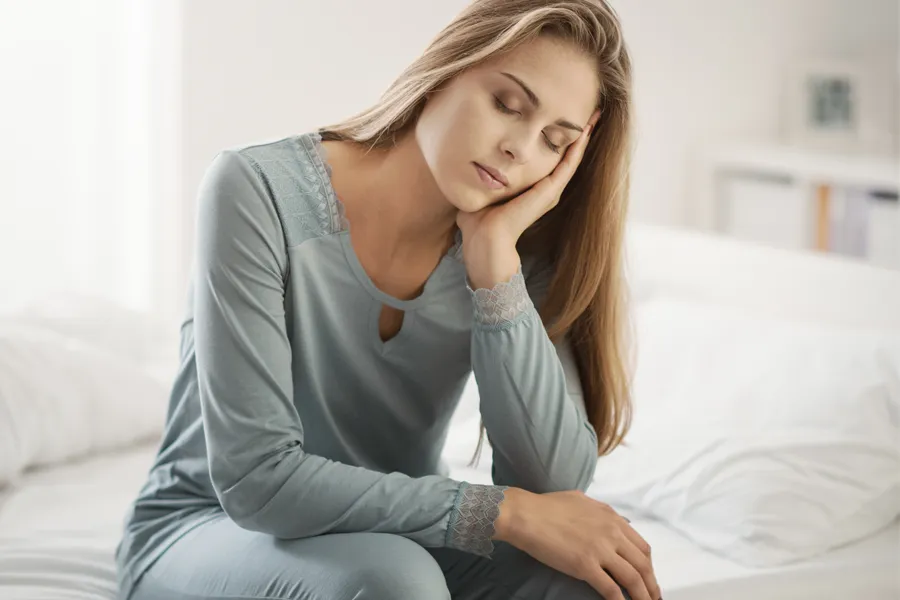Depression-Clinic A woman sits on the edge of her bed with her head in her hands. Schedule treatment for depression from Morgan Burns, APRN in Central Florida.