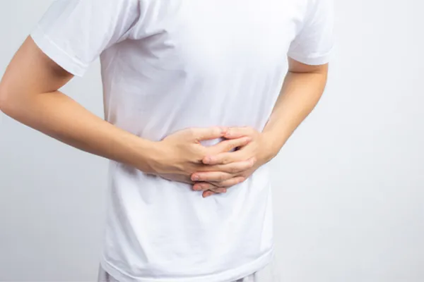 Irritable-Bowel-Syndrome-Clinic A person holding their stomach in visible discomfort against a plain background. Morgan Burns, APRN treats irritable bowel syndrome with functional medicine in Central Florida.