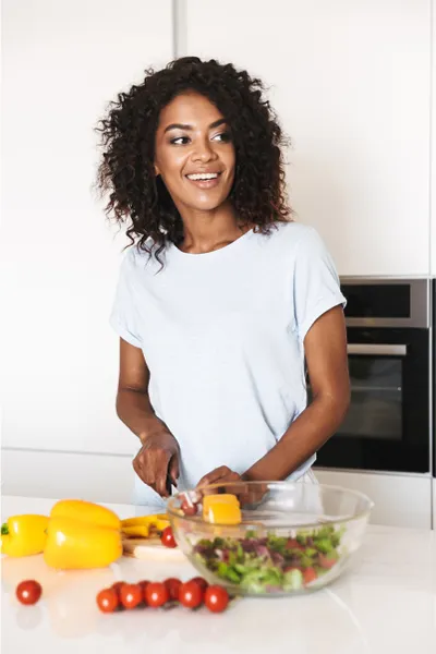 Irritable-Bowel-Syndrome-Treatment Image featuring a smiling woman chopping vegetables for a salad in a bright, white kitchen. Morgan Burns, APRN offers Irritable Bowel Syndrome Treatment and Digestive Support in Central Florida.