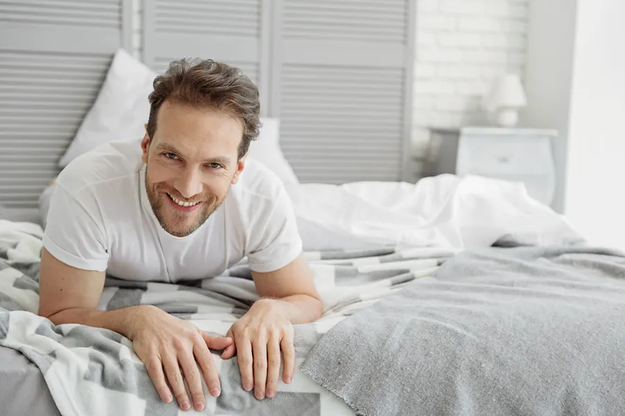 Low-Libido-in-Men-Doctor A dirty-blonde haired man lays on his stomach in bed smiling. Schedule treatment for low libido in men from Morgan Burns, APRN in Central Florida.