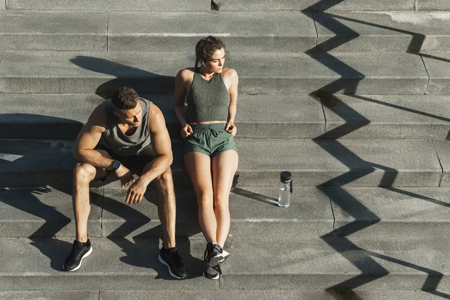 Medical-Weight-Loss-Doctor A couple in gray and green track clothes resting after a workout on stone steps, happy with their weight loss plans from Morgan Burns, APRN in Central Florida.
