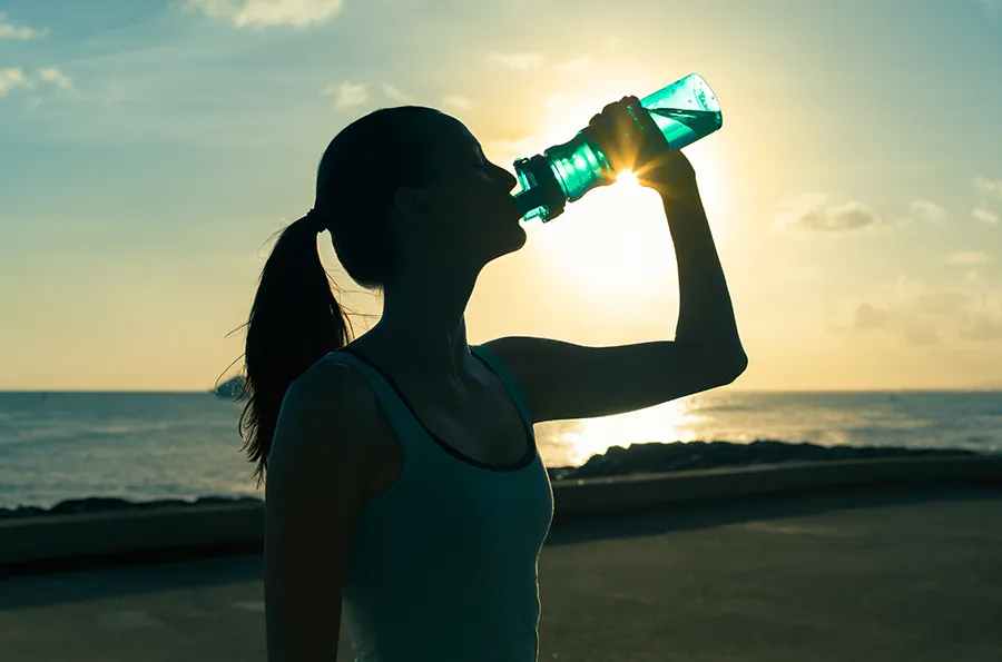 Natural-Detoxification-Clinic A woman hydrates during a beach run at sunset. Schedule natural detoxification treatment from Morgan Burns, APRN in Central Florida.