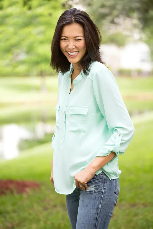 Perimenopause-Treatment A middle-aged brunette woman in a light green button-up shirt stands outside smiling, happy with her perimenopause treatment from Morgan Burns, APRN in Central Florida.