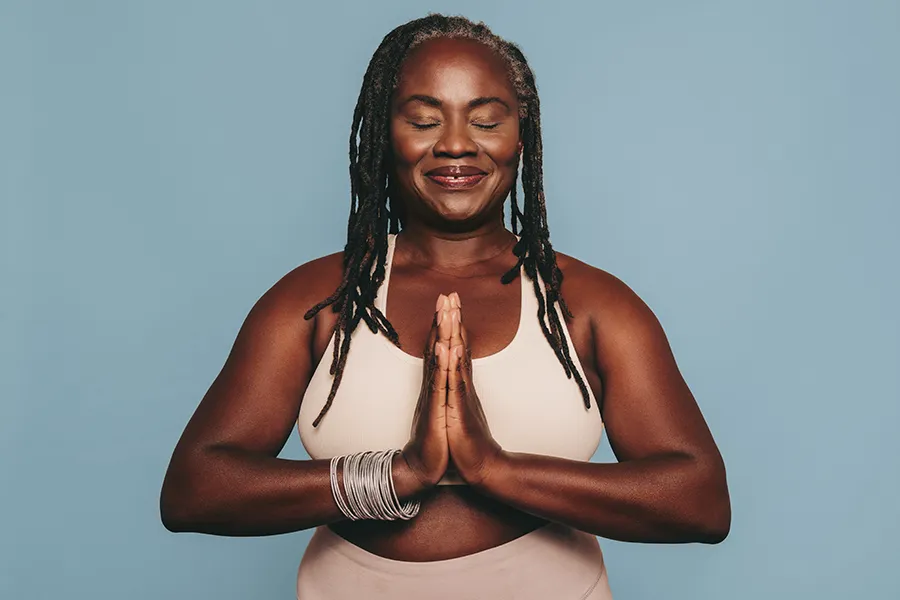 Pre-Diabetes-Specialist-2 An older black woman with closed eyes holds her hands together in a yoga pose. Get treatment for pre-diabetes from Morgan Burns, APRN in Central Florida.