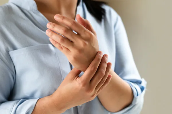 Rheumatoid-Arthritis-Clinic Close up of a woman in a blue blouse rubbing her wrist. Get rheumatoid arthritis treatment from Morgan Burns, APRN in Central Florida.