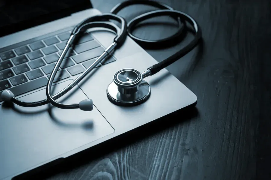 Telemedicine-Doctor An open laptop with a stethoscope lying on it on a wooden table, symbolizing telemedicine care from Morgan Burns, APRN in Central Florida.