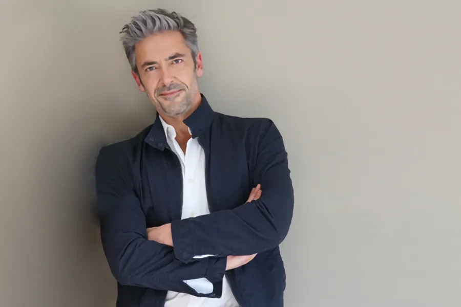 Testosterone-Low-T-Solutionsn-Clinic A middle-aged man in a white shirt and dark blue jacket leans against a gray wall smiling. Get testosterone for Low T from Morgan Burns, APRN in Central Florida.