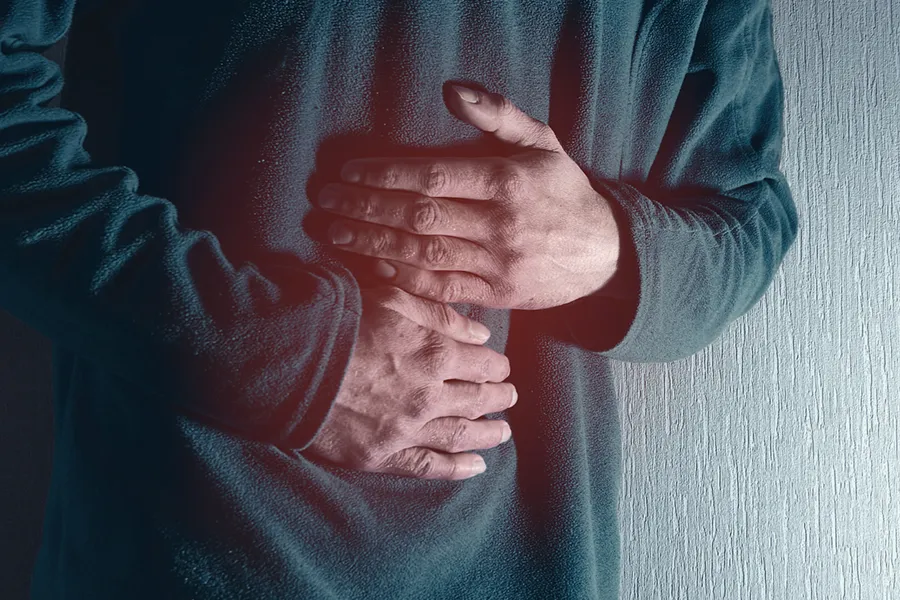 Ulcerative-Colitis-Clinic Close-up of the midsection of a man in a green sweater clutching his gut in pain. Get treatment for Ulcerative Colitis from Morgan Burns, APRN in Central Florida.