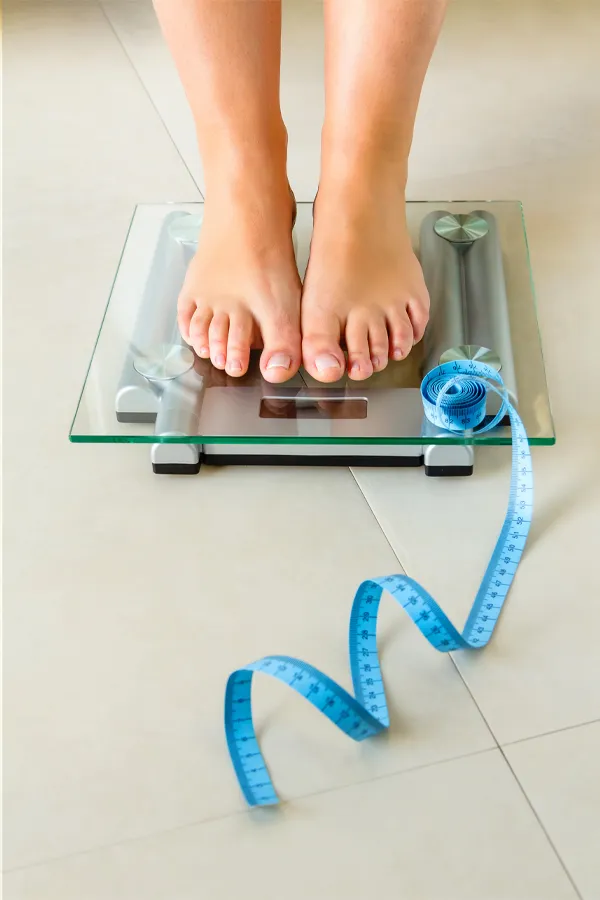 Weight-Loss-Resistance-Treatment Close-up of a woman's feet standing on a scale, with measuring tape by her toes, getting treatment for weight loss resistance from Morgan Burns, APRN in Central Florida.
